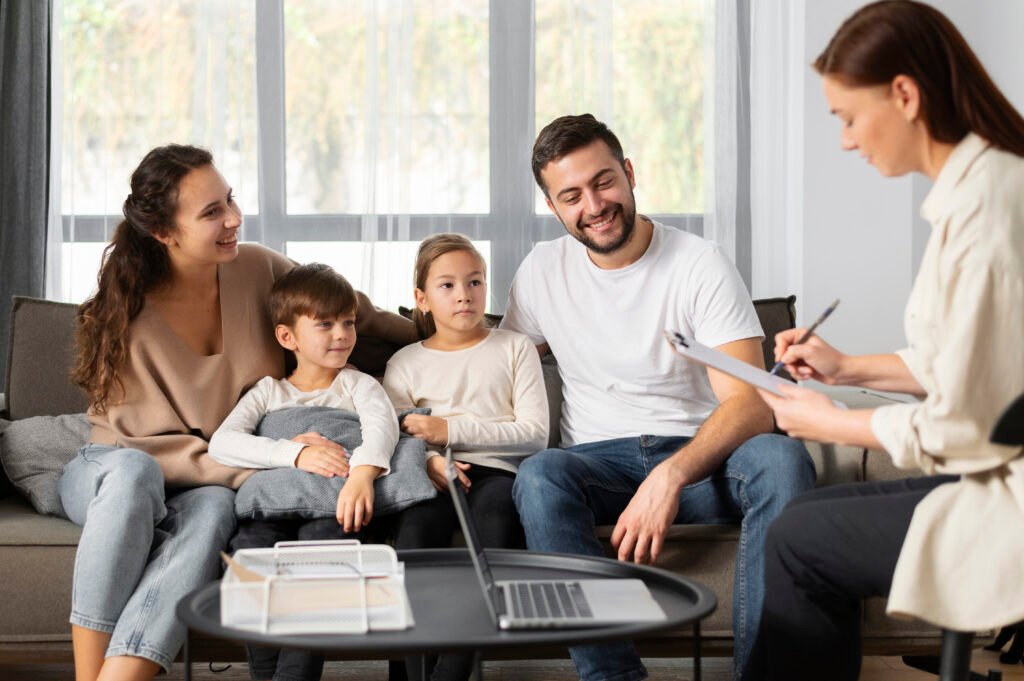 Eltern sitzen mit ihren beiden Kindern auf dem Sofa und sprechen mit einer Beraterin, die sich Notizen macht