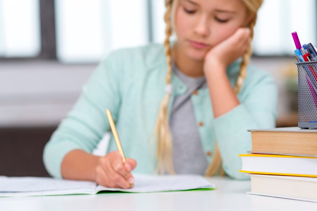 Grundschülerin schreibt konzentriert in ihr Heft, daneben ein Stapel Bücher und ein Stiftebecher